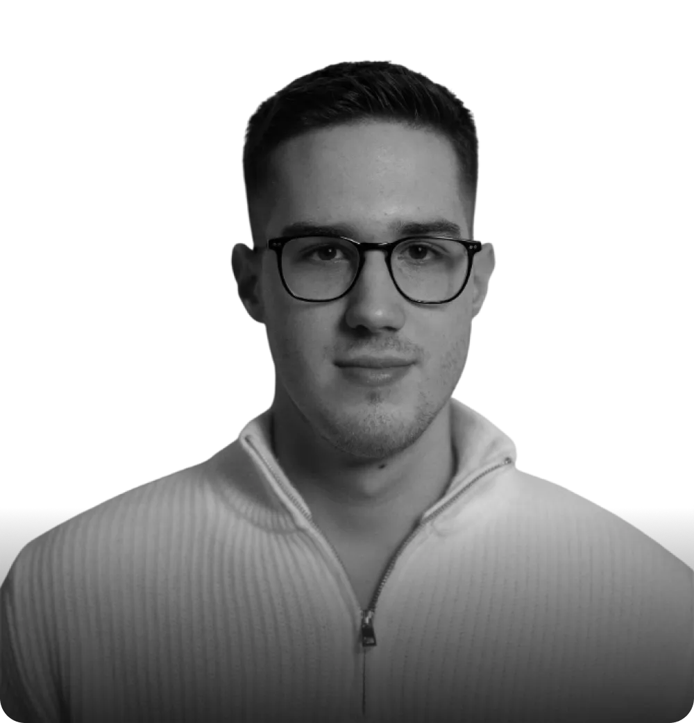 Young man with short hair and glasses wearing a light-colored zip-up sweater, looking directly at the camera.